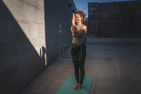 Foto de Una mujer caucásica adulta que practica yoga se estira en el día de verano al aire libre en la ciudad frente a la pared con sombra y sol estilo de vida saludable concepto de autocuidado - Imagen libre de derechos