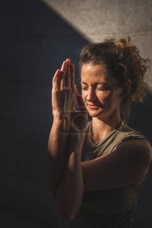 Photo for One adult caucasian woman doing yoga practice stretch in summer day outdoor in the city in front of the wall with shadow and sun healthy lifestyle well-being concept self care - Royalty Free Image