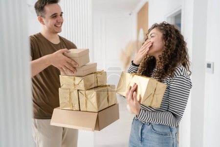 Téléchargez les photos : Femme jeune adulte caucasien femme debout à la maison avec boîte cadeau cadeaux tenant dans les mains tandis que son petit ami ou mari homme donner boîtes heureux sourire vraies personnes célèbrent concept surprise - en image libre de droit