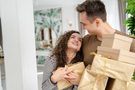 Téléchargez les photos : Femme jeune adulte caucasien femme debout à la maison avec boîte cadeau cadeaux tenant dans les mains tandis que son petit ami ou mari homme donner boîtes heureux sourire vraies personnes célèbrent concept d'amour surprise - en image libre de droit