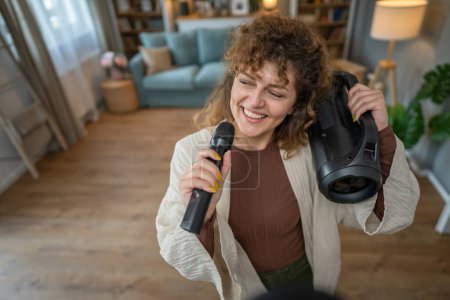 Téléchargez les photos : Une femme jeune adulte tenir microphone à la maison heureux sourire chanter danse - en image libre de droit