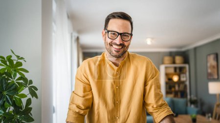 Téléchargez les photos : Un homme adulte caucasien mâle avec barbe et lunettes se tenir à la maison heureux sourire copie espace - en image libre de droit