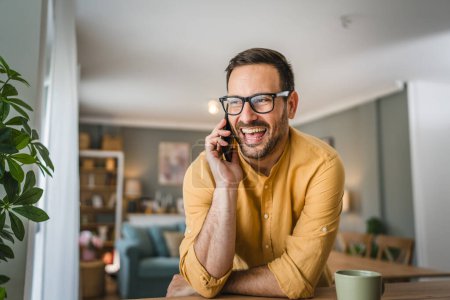 Foto de One man adult caucasian male with beard and eyeglasses stand at home happy smile use mobile phone smartphone to make a call talking copy space - Imagen libre de derechos