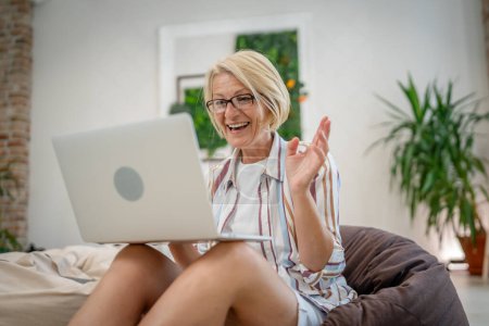 Téléchargez les photos : Une femme mature caucasienne utilisation ordinateur portable pour le travail ou pour naviguer sur Internet en ligne à l'intérieur au bureau ou à la maison de vraies personnes copier l'espace - en image libre de droit