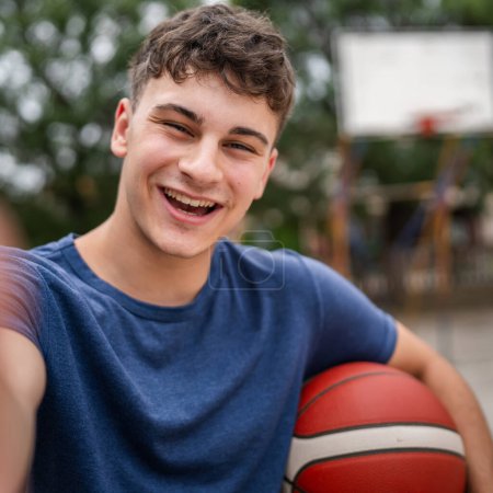 Photo for One teenager caucasian male caucasian young man stand on basketball court with ball in the evening ready to play game copy space real person user generated content - Royalty Free Image