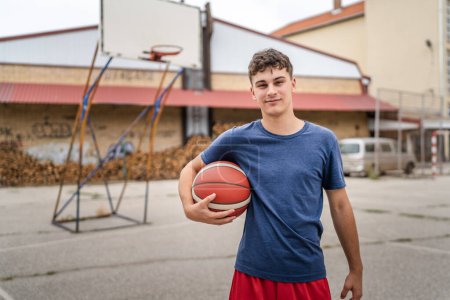 Photo for One teenager caucasian male caucasian young man stand on basketball court with ball in the evening ready to play game copy space real person - Royalty Free Image