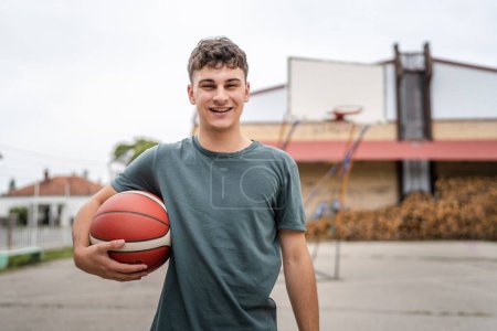 Téléchargez les photos : Un adolescent caucasien mâle caucasien jeune homme debout sur le terrain de basket-ball avec balle dans la soirée prêt à jouer copie jeu espace personne réelle - en image libre de droit
