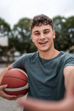 Téléchargez les photos : Un adolescent caucasien mâle caucasien jeune homme debout sur le terrain de basket-ball avec balle dans la soirée prêt à jouer espace de copie de jeu contenu généré par l'utilisateur personne réelle - en image libre de droit