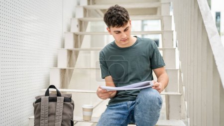 Téléchargez les photos : Un jeune homme adolescent étudiant caucasien avec des livres lire étude sur le campus dans la journée assis sur escalier éducation concept copier l'espace - en image libre de droit