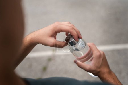 Téléchargez les photos : Gros plan sur les mains midsection de l'homme caucasien inconnu adolescent bouteille en plastique ouverte d'eau en plein air dans la journée ensoleillée - en image libre de droit