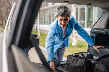 Photo for One senior beautiful woman travel concept female take luggage baggage suitcase and other stuff and belongings from the back of her car while moving or arrive to destination real people copy space - Royalty Free Image