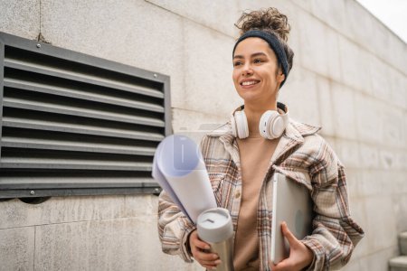 Photo for One woman young adult female student go to class outdoor hold laptop computer cup of coffee and work material real person coy space happy smile confident with headphones in day - Royalty Free Image