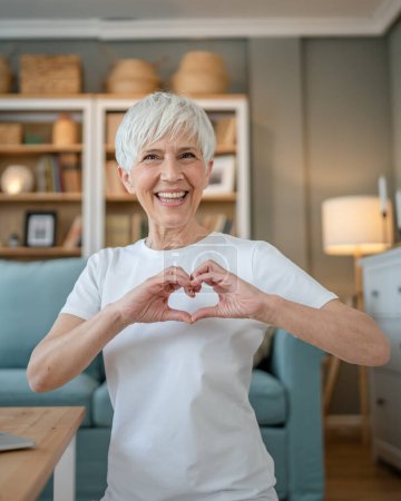 Photo for Healthy senior caucasian woman showing hart hand gesture health love happy smile while sit at home looking to the camera smiling copy space - Royalty Free Image