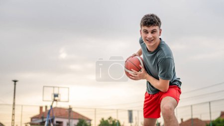 Photo for One teenager caucasian male caucasian young man stand on basketball court with ball in the evening ready to play game copy space real person - Royalty Free Image