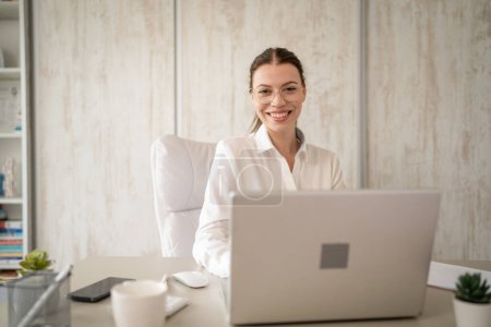 Photo for One woman female caucasian entrepreneur businesswoman or secretary sitting at her office at desk work on laptop computer happy smile wear white shirt copy space - Royalty Free Image