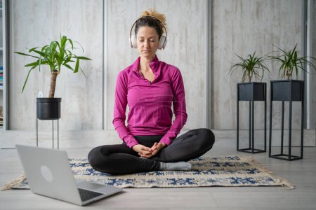 Photo for One woman adult caucasian female millennial using headphones and laptop computer for online guided meditation practicing mindfulness yoga with eyes closed on the floor at home real people copy space - Royalty Free Image
