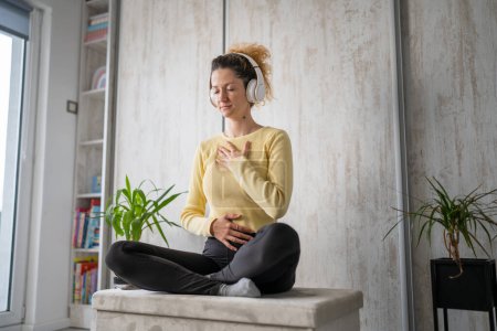 eine erwachsene kaukasische Millennial mit Kopfhörern für Online-geführte Meditation praktiziert Achtsamkeits-Yoga mit geschlossenen Augen auf dem Boden zu Hause echte Menschen kopieren Weltraum-Selbstversorgungskonzept