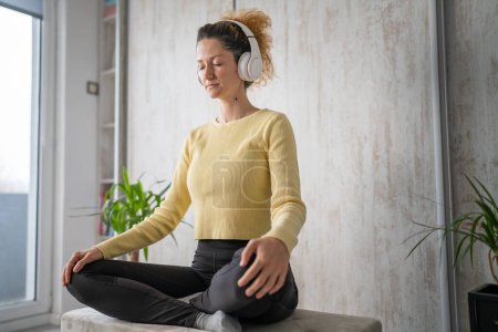 eine erwachsene kaukasische Millennial mit Kopfhörern für Online-geführte Meditation praktiziert Achtsamkeits-Yoga mit geschlossenen Augen auf dem Boden zu Hause echte Menschen kopieren Weltraum-Selbstversorgungskonzept