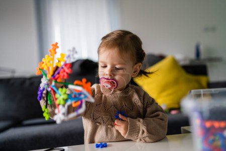 Foto de Un niño pequeño niña caucásica pequeño niño con chupete de pezón jugando en la mesa en casa solo infancia creciendo espacio de copia concepto - Imagen libre de derechos