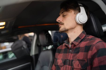 Photo for One man young adult caucasian male sit in the car on the seat with headphones listen guided meditation relaxation practicing mindfulness or listen music or podcast real people copy space eyes closed - Royalty Free Image