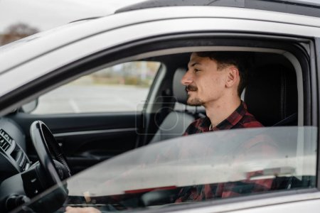 Téléchargez les photos : Un homme caucasien mâle avec les cheveux bruns et les moustaches assis dans une voiture adulte conducteur porter chemise tout en conduisant concept de transport automobile personnes réelles copier l'espace - en image libre de droit