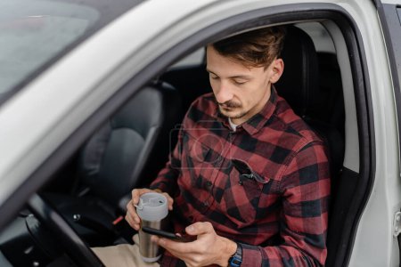 Photo for One man caucasian male with mustaches sit in the car take a brake on road-trip hold cup of coffee use mobile phone smartphone for sms texting or navigation app real people copy space - Royalty Free Image