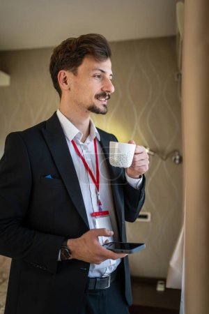 Téléchargez les photos : Un homme adulte caucasien costume masculin avec moustaches et barbe homme d'affaires dans la chambre d'hôtel tenir tasse de café avant ou après le travail en prenant un espace de copie de personnes réelles frein - en image libre de droit
