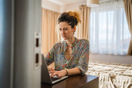 Téléchargez les photos : Une femme adulte caucasienne travail sur ordinateur portable dans la chambre ou la chambre d'hôtel - en image libre de droit