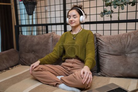 Téléchargez les photos : One woman adult caucasian female using headphones for online guided meditation practicing mindfulness yoga with eyes closed on the sofa bed at home real people self care concept copy space - en image libre de droit