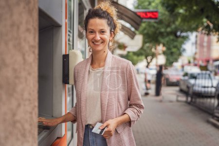 Foto de Mujer usando tarjeta de crédito y retirando efectivo en el cajero automático - Imagen libre de derechos