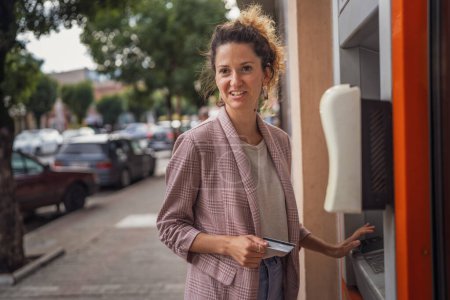Téléchargez les photos : Femme utilisant une carte de crédit et retirant de l'argent au guichet automatique - en image libre de droit