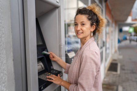 Téléchargez les photos : Femme utilisant une carte de crédit et retirant de l'argent au guichet automatique - en image libre de droit