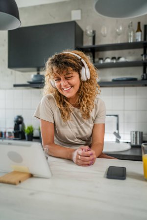 Photo for One caucasian woman with curly hair sit at home use digital tablet and headphones to watch movie or series online stream or to have video call happy smile have a good time copy space - Royalty Free Image