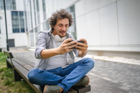 Photo for One caucasian man sit outdoor take a brake happy smile play video games leisure activity having fun hold mobile phone use smartphone have fun online copy space adult male - Royalty Free Image