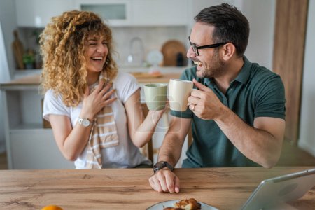Téléchargez les photos : Jeune couple caucasien homme et femme mari et femme profiter d'une tasse de thé ou de café le matin à la maison sourire heureux tous les jours matin routine vraies personnes - en image libre de droit