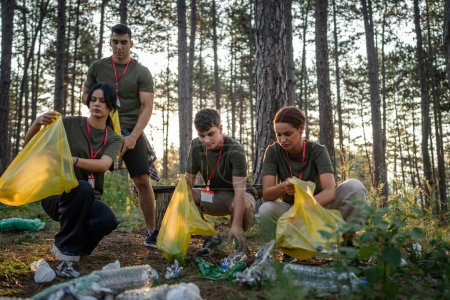 Téléchargez les photos : Groupe d'amis adolescents génération Z hommes et femmes caucasiens femmes ramasser des déchets bouteilles en plastique et du papier de la forêt nettoyage de la nature dans la journée ensoleillée écologie concept de soins de l'environnement - en image libre de droit