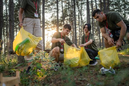 Téléchargez les photos : Groupe d'amis adolescents génération Z hommes et femmes caucasiens femmes ramasser des déchets bouteilles en plastique et du papier de la forêt nettoyage de la nature dans la journée ensoleillée écologie concept de soins de l'environnement - en image libre de droit