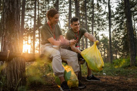 Photo for Couple or teenage friends gen Z male and female caucasian man woman picking up waste garbage plastic bottles and paper from forest cleaning up nature in sunny day environmental care ecology concept - Royalty Free Image