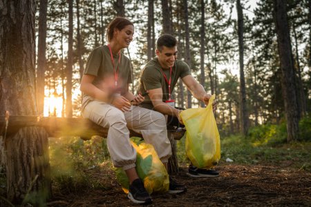 Photo for Couple or teenage friends gen Z male and female caucasian man woman picking up waste garbage plastic bottles and paper from forest cleaning up nature in sunny day environmental care ecology concept - Royalty Free Image