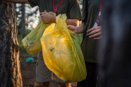 Téléchargez les photos : Mains d'un groupe d'amis génération Z caucasien mâle et femelle ramasser des déchets bouteilles en plastique et du papier de la forêt nettoyage de la nature dans la journée ensoleillée écologie concept de soins de l'environnement - en image libre de droit