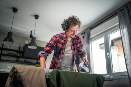 Photo for One man ironing clothes at home hold iron on shirt on board household chores concept adult male in 30s living in the apartment alone doing housework copy space - Royalty Free Image