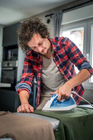 Photo for One man ironing clothes at home hold iron on shirt on board household chores concept adult male in 30s living in the apartment alone doing housework copy space - Royalty Free Image
