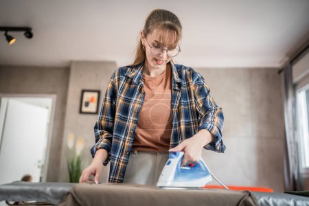 Photo for One young woman teenage student ironing clothes at home foo the first time hold iron on shirt on board household chores concept female living in the apartment alone doing housework copy space - Royalty Free Image