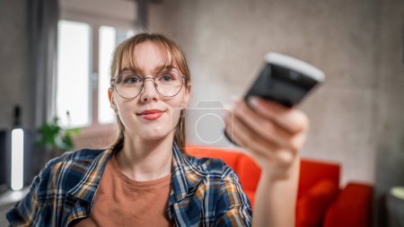 Photo for One young caucasian woman use remote control for TV or air-condition - Royalty Free Image