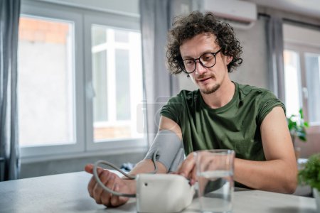 Téléchargez les photos : Un homme caucasien homme assis à la table de contrôle de bureau mesurer la pression artérielle à la maison concept de soins de santé personne réelle - en image libre de droit