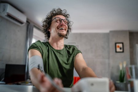 Téléchargez les photos : Un homme caucasien homme assis à la table de contrôle de bureau mesurer la pression artérielle à la maison concept de soins de santé personne réelle - en image libre de droit