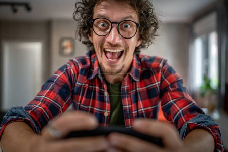 Photo for Caucasian man sit at home play video games on smartphone mobile phone - Royalty Free Image