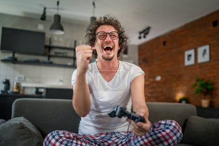 Téléchargez les photos : Adulte homme caucasien mâle jouer console jeux vidéo à la maison tenir joystick contrôleur avoir plaisir loisirs joie et gagner et succès concept copier espace - en image libre de droit