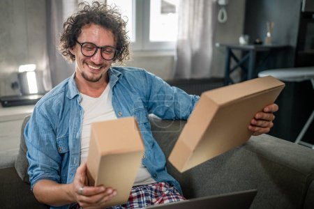 Photo for One caucasian male adult man sit at home on the sofa bed receiving package by post product he ordered online or special gift happy smile real people delivery service concept - Royalty Free Image