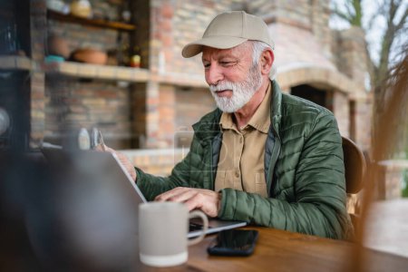 Téléchargez les photos : Un homme caucasien senior homme avec barbe assis en plein air dans la journée avec ordinateur portable faire des achats en ligne acheter des trucs détenir carte de crédit pensionné profiter de son espace de copie de retraite personne réelle - en image libre de droit